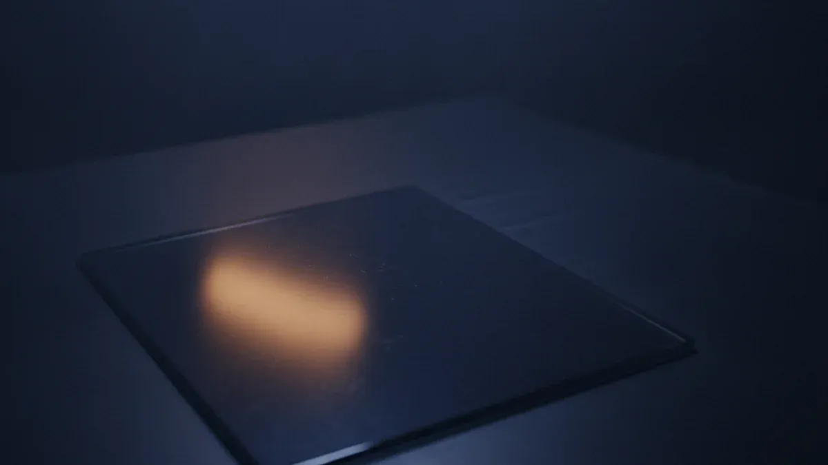 A dark reflective slab of glass lies flat on a table, its surface completely blank, holding only one soft warm reflection