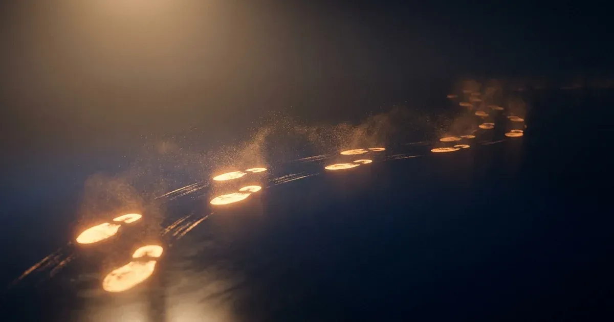 A curved trail of warm glowing points of light runs across a dark misty surface and dissolves into fine dust towards the back