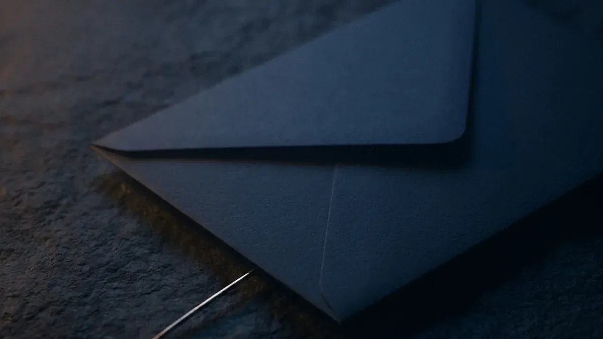 A plain dark envelope lies closed on a stone surface with a thin taut wire running out from beneath its edge and disappearing into shadow