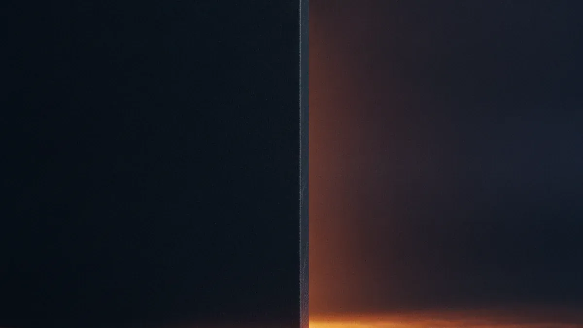 A smooth dark stone wall stands across a shallow channel of warm light, the light piling up against the near side with only a thin trickle seeping past the lower edge